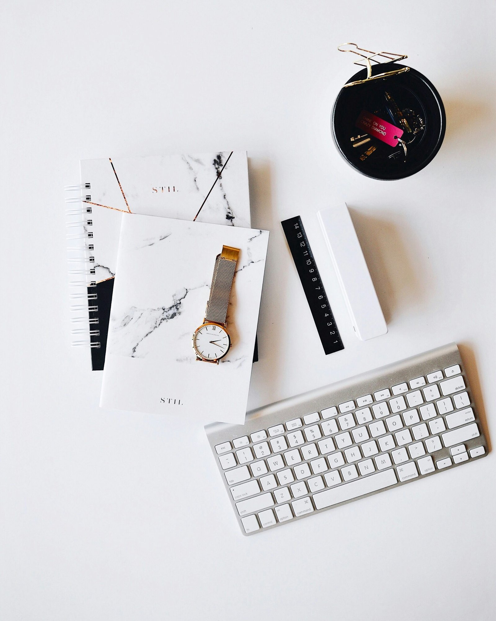 Apple Magic Keyboard near round gold-colored analog watch with silver-colored mesh band with notebook on white surface photography